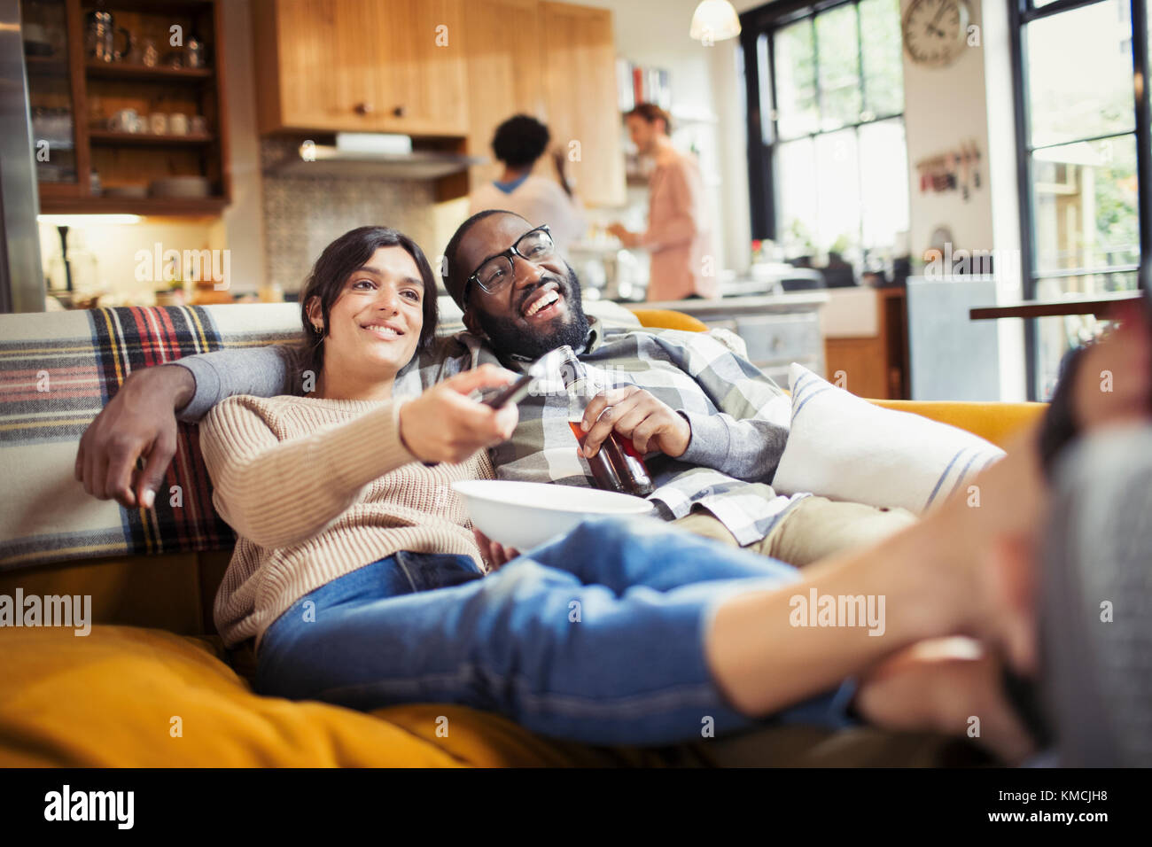 Lächelndes junges Paar, das Fernsehen schaut, Bier trinkt und Popcorn auf dem Sofa im Wohnzimmer isst Stockfoto