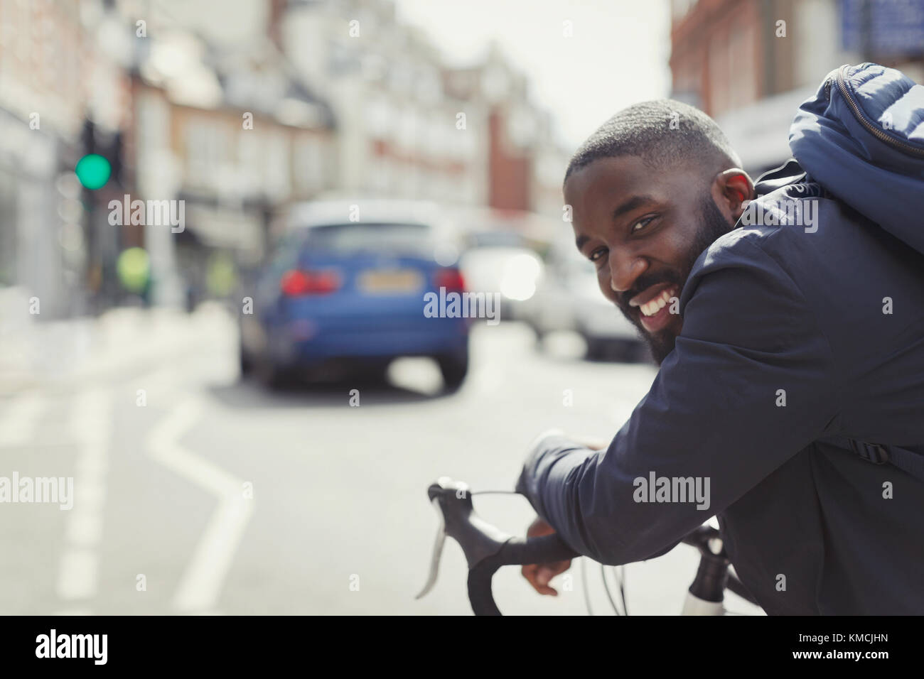 Lächelnder junger Geschäftsmann pendelt, Fahrrad auf sonniger Stadtstraße reitet Stockfoto