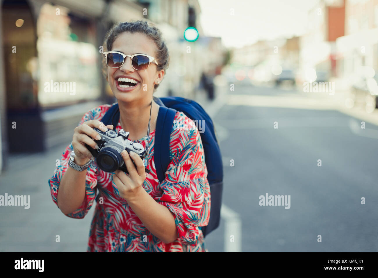 Portrait lachende, begeisterte junge Touristin in Sonnenbrillen, die mit Kamera auf der städtischen Straße fotografiert Stockfoto
