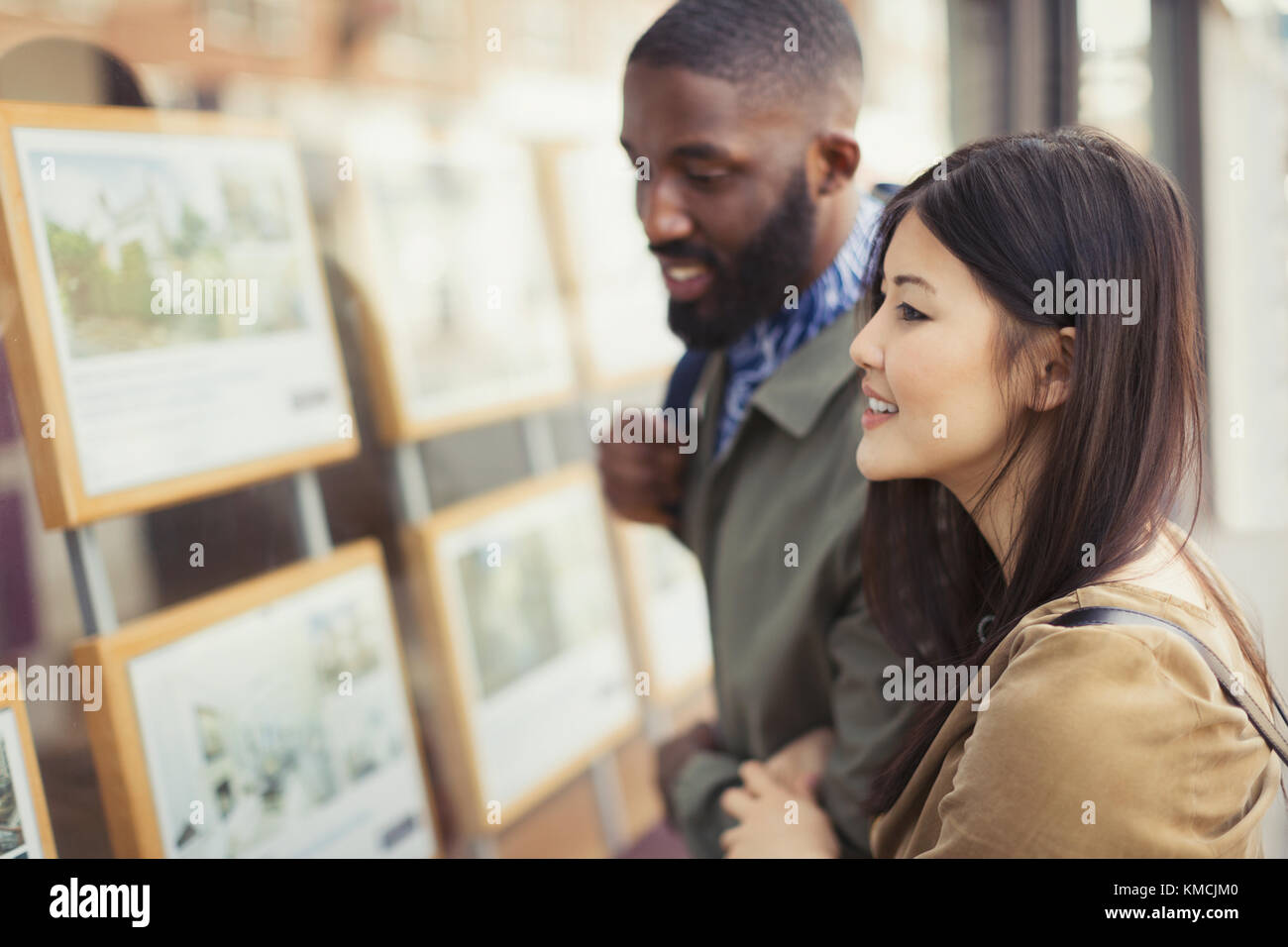 Lächelndes junges Paar, das Immobilien-Angebote im Schaufenster ansieht Stockfoto