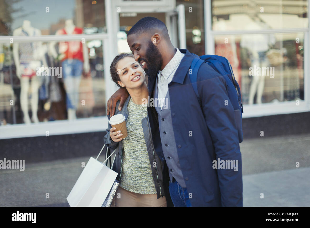 Liebevolles junges Paar mit Kaffee und Einkaufstasche vor dem Ladenlokal Stockfoto