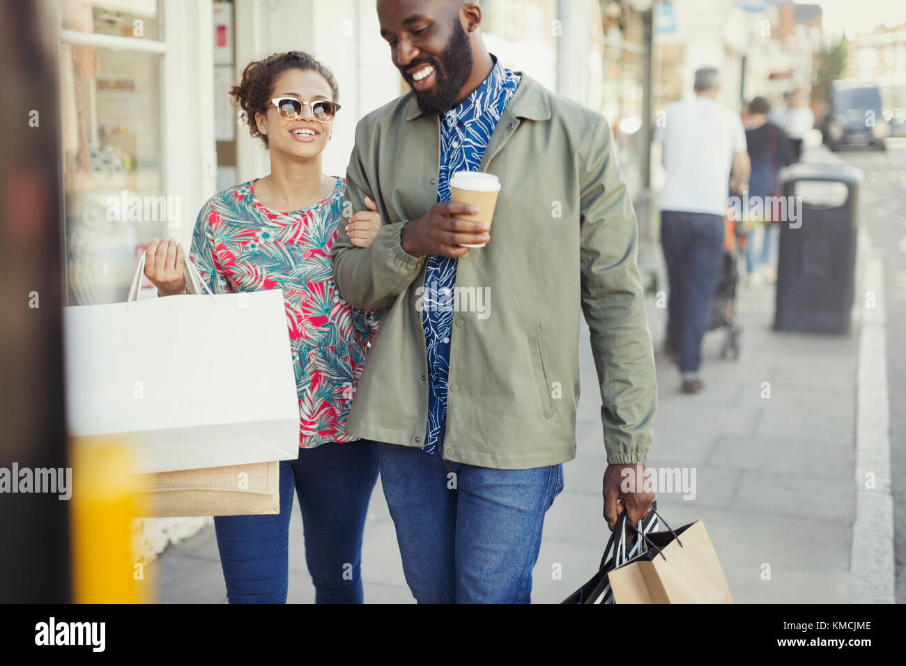 Lächelndes junges Paar mit Kaffee und Einkaufstaschen storefront Stockfoto