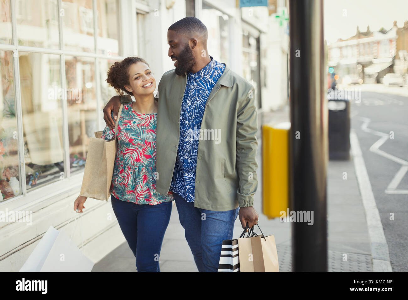 Liebevolles junges Paar mit Einkaufstaschen, die entlang der städtischen Schaufenster laufen Stockfoto
