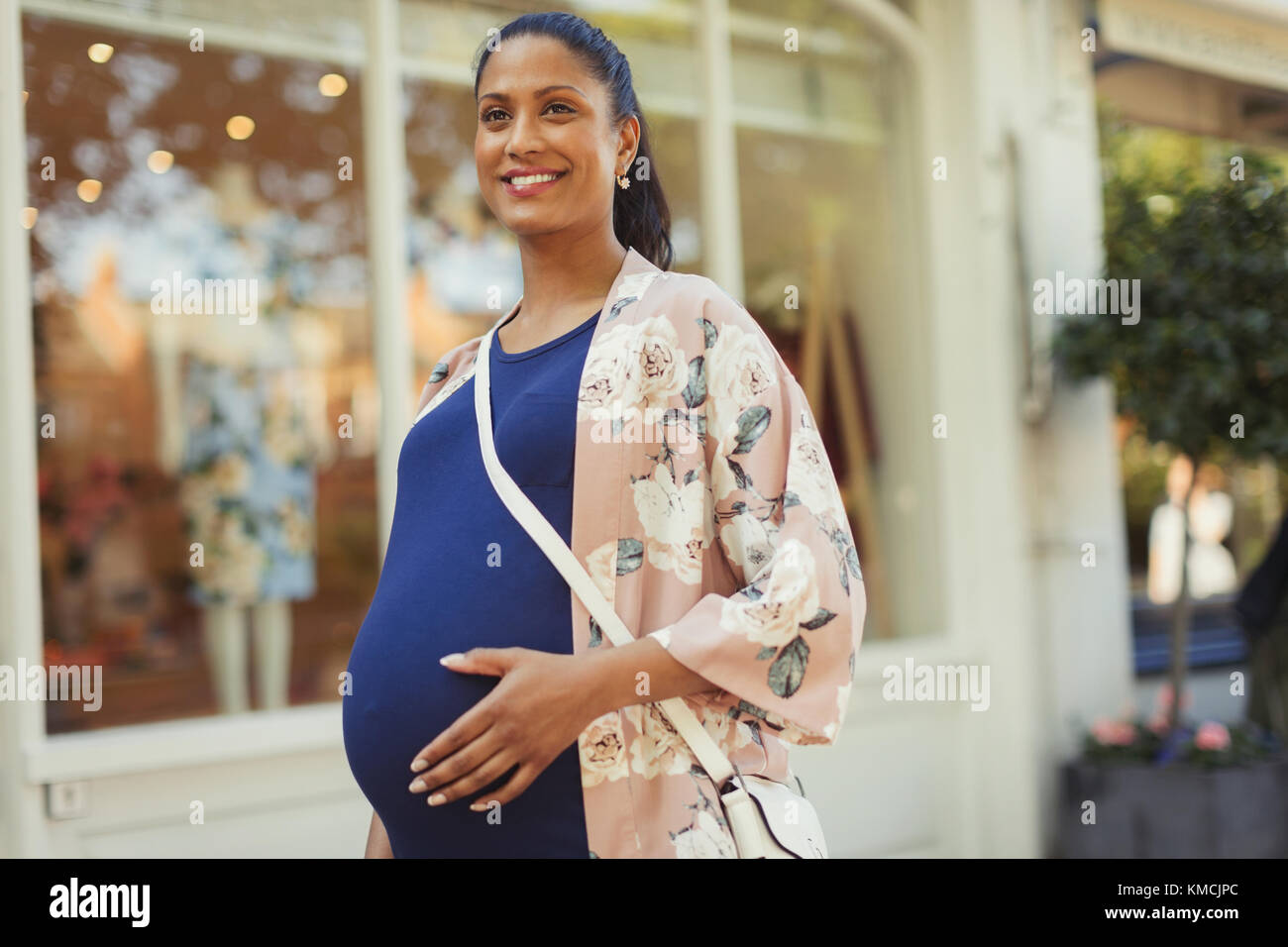 Portrait lächelnde schwangere Frau außerhalb Schaufenster Stockfoto