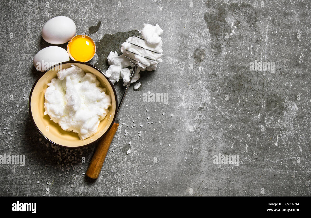 Eier in einer Schüssel mit einem Schneebesen Schlagsahne. Auf einem Stein Hintergrund. freier Platz für Text. top View Stockfoto