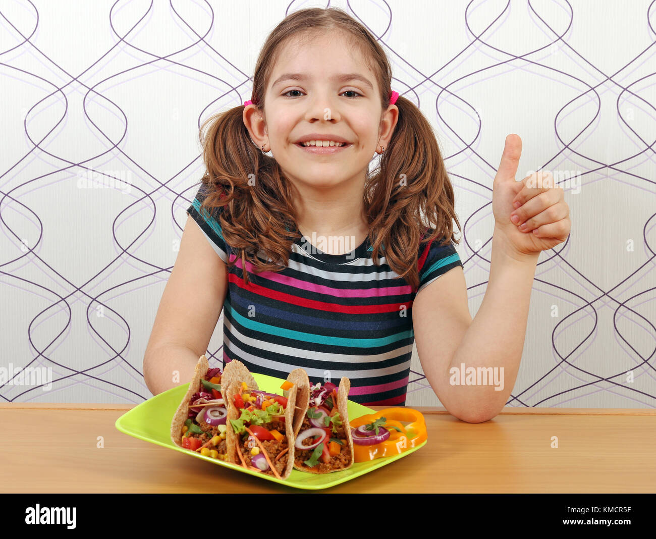 Glückliche kleine Mädchen mit Tacos und Daumen hoch Stockfoto
