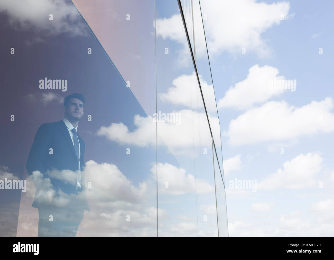 Geschäftsmann mit Blick aus dem modernen Bürofenster auf den blauen Himmel und Wolken Stockfoto