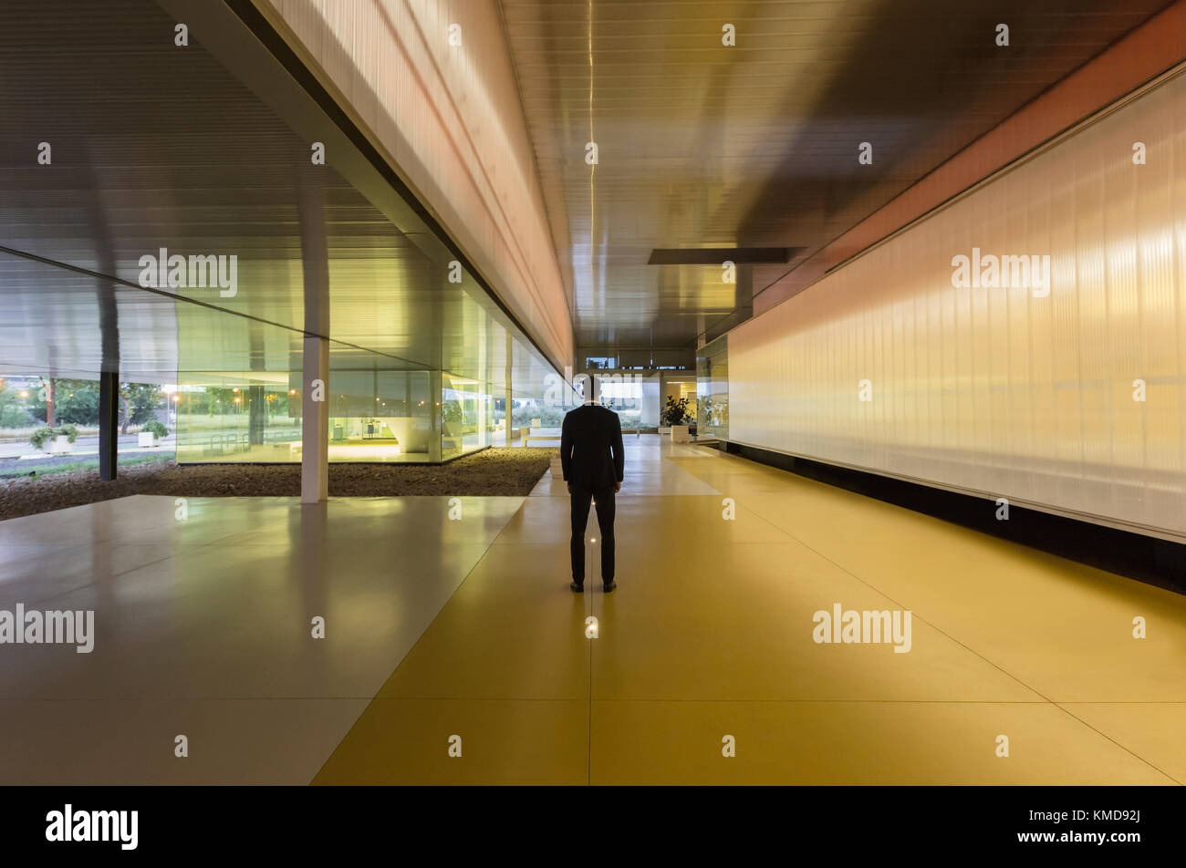 Ein Geschäftsmann steht in einem beleuchteten, modernen Büroflur in der Lobby Stockfoto