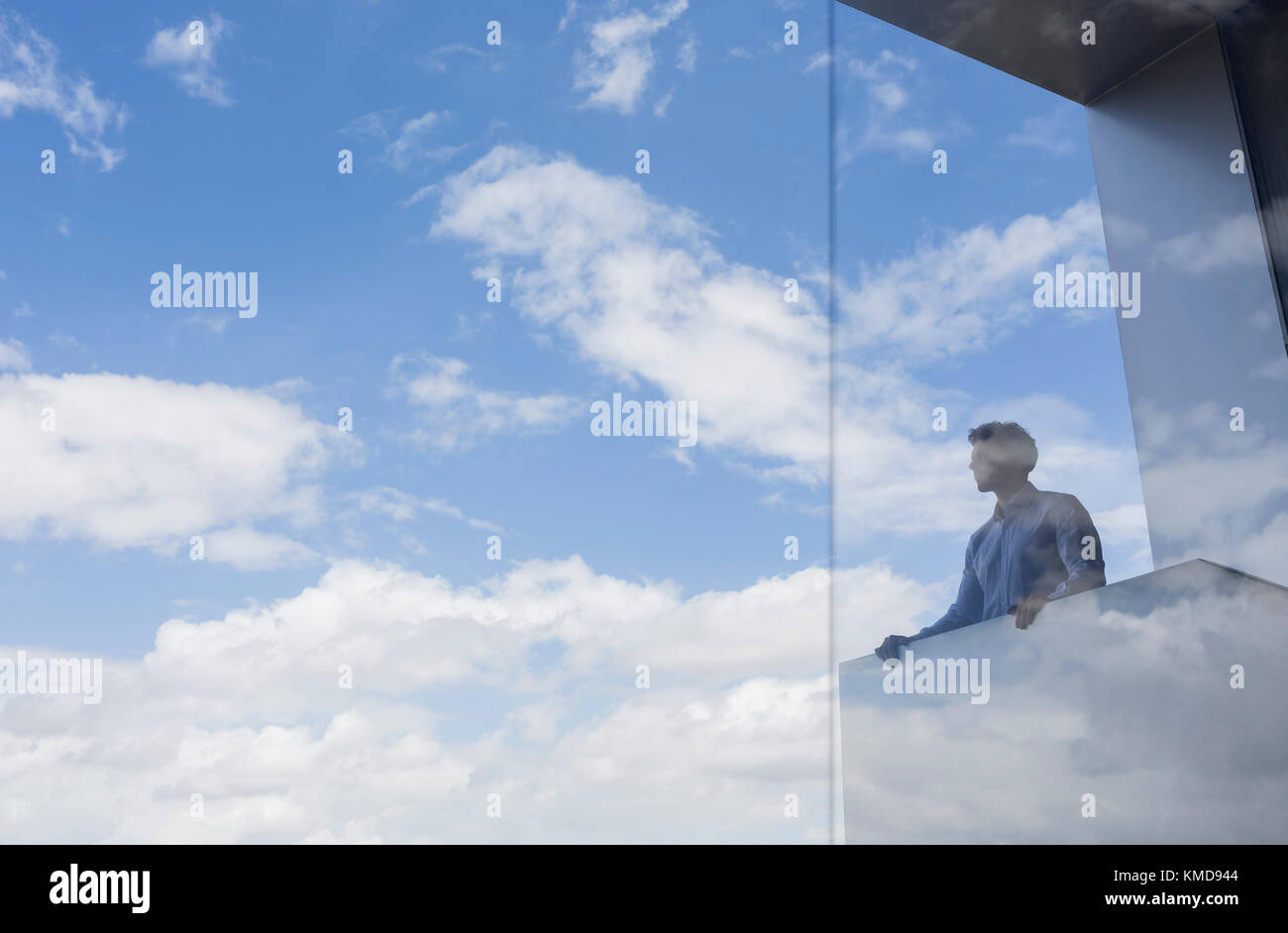 Nachdenklicher Geschäftsmann, der auf einem modernen Balkon steht und auf sonniges Blau blickt Himmel und Wolken Stockfoto