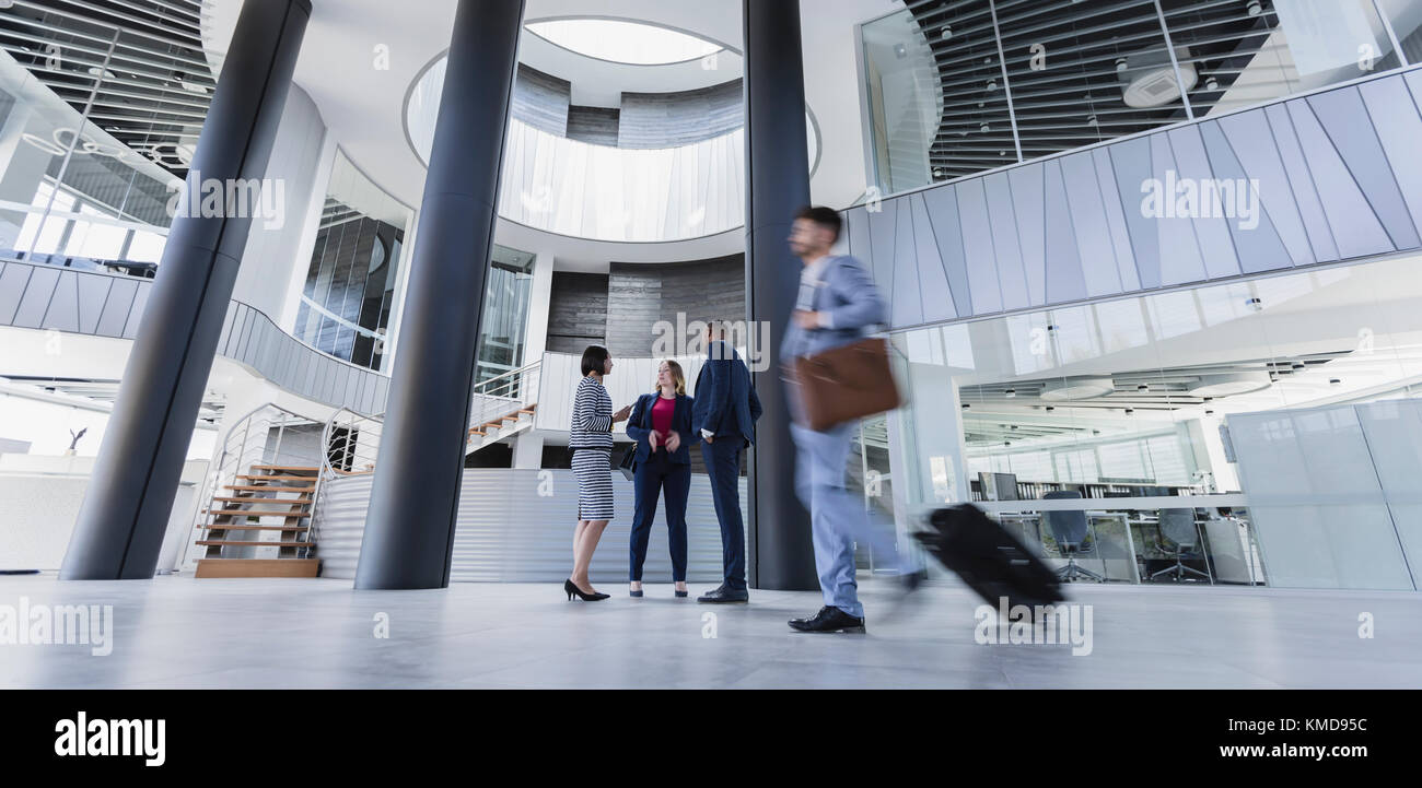 Geschäftsleute reden und ziehen Koffer in der architektonischen, modernen Bürolobby Stockfoto