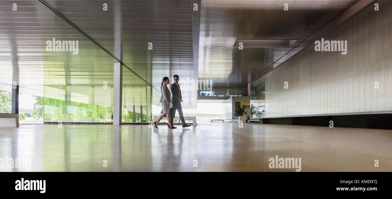 Geschäftsmann und Geschäftsfrau, die in der modernen Bürolobby spazieren gehen Stockfoto