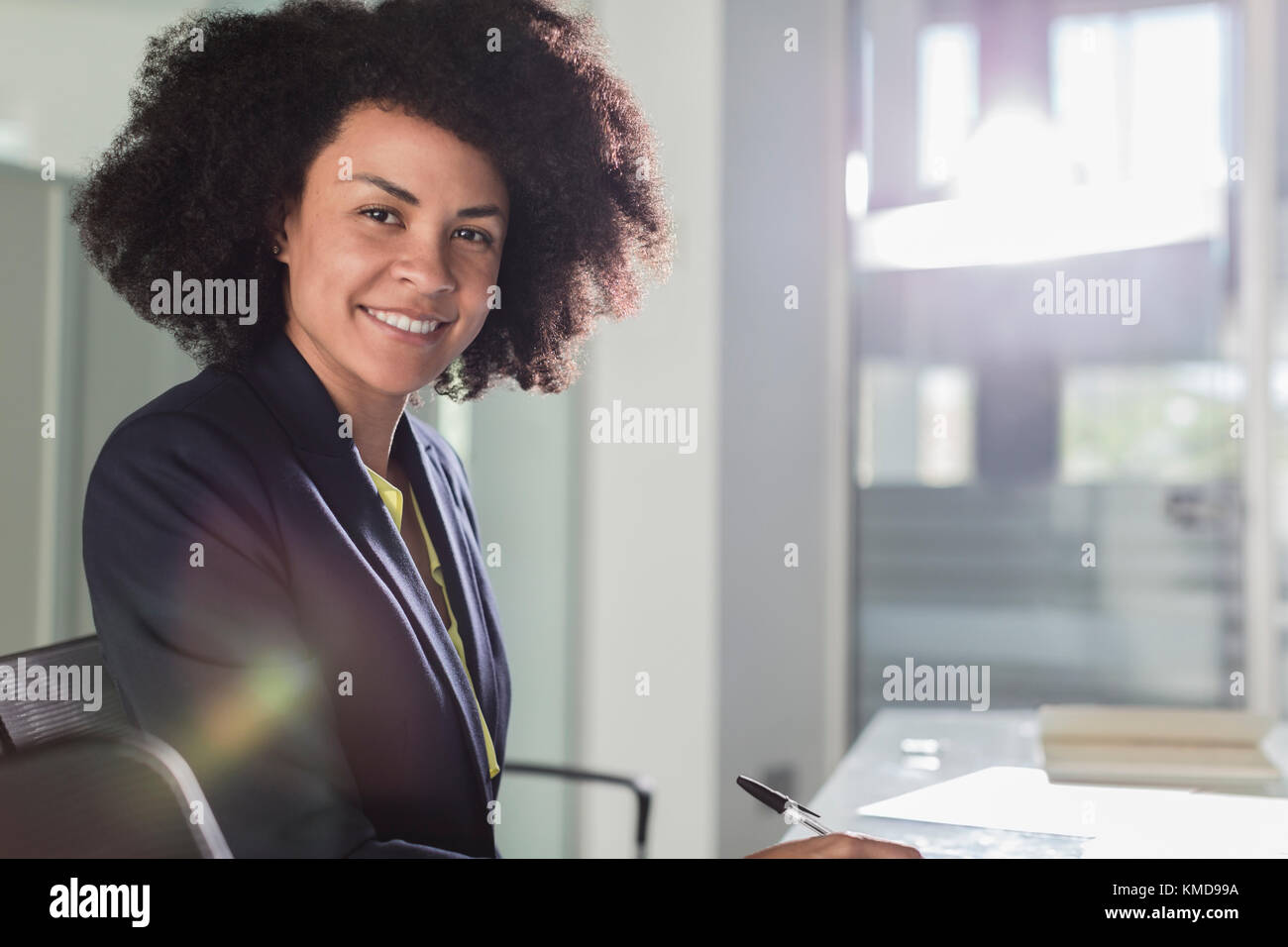Portrait lächelnd, selbstbewusste Geschäftsfrau, die im sonnigen Büro arbeitet Stockfoto