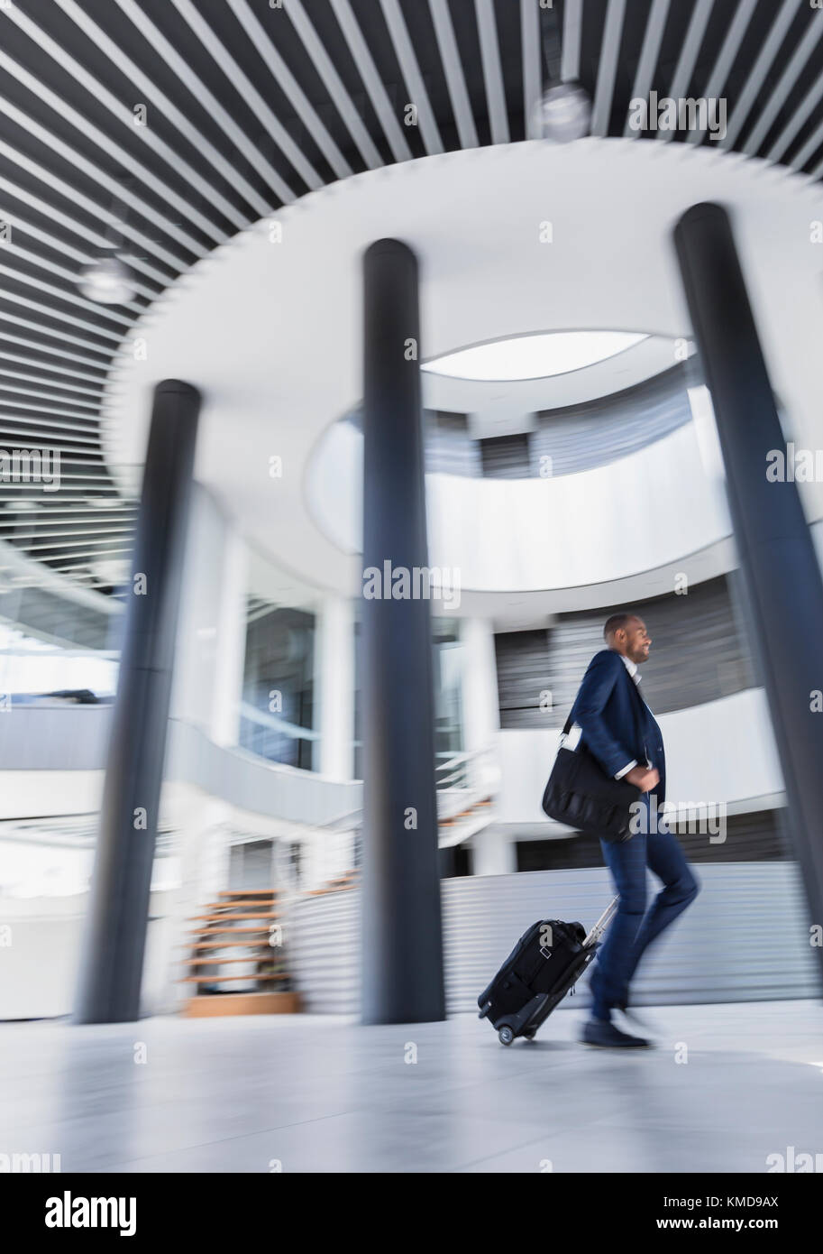 Geschäftsmann eilt, zieht Koffer in der architektonischen, modernen Bürolobby Stockfoto