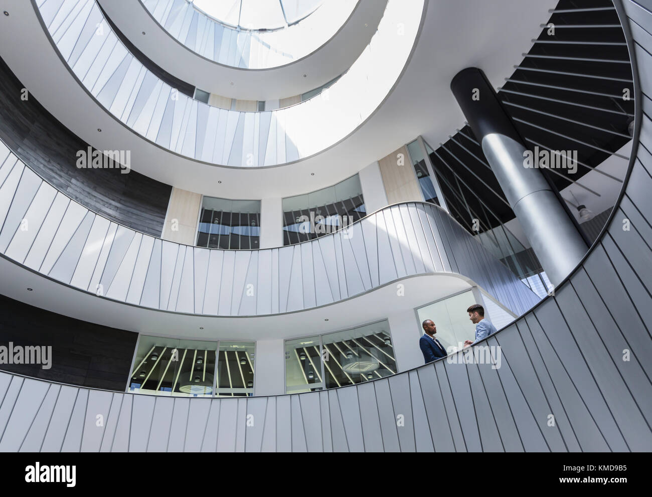 Geschäftsleute, die über einen architektonischen, modernen Atrium-Balkon im Büro sprechen Stockfoto