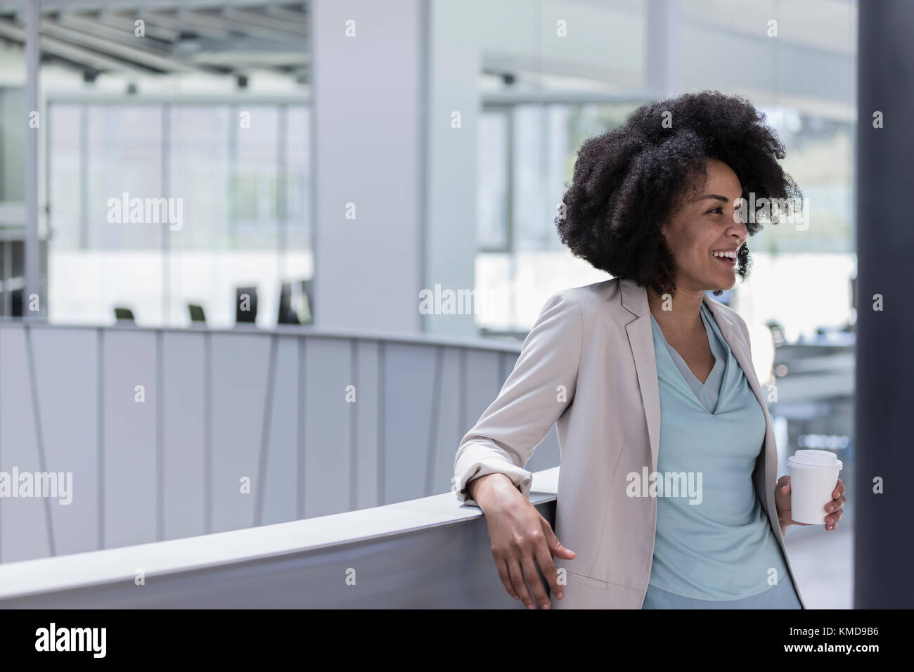 Lächelnde Geschäftsfrau trinkt Kaffee an der Bürogeländer Stockfoto