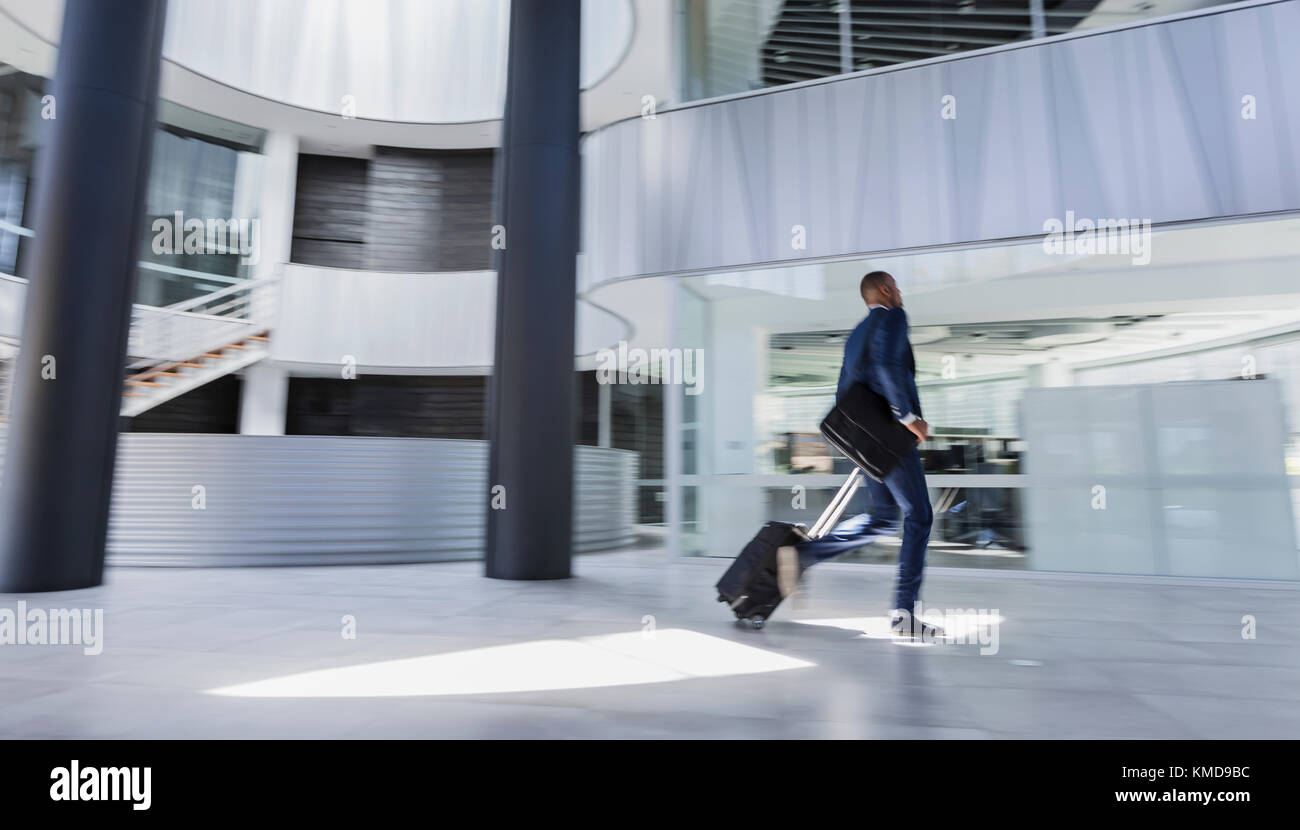 Geschäftsmann eilt und zieht Koffer in die moderne Bürolobby Stockfoto