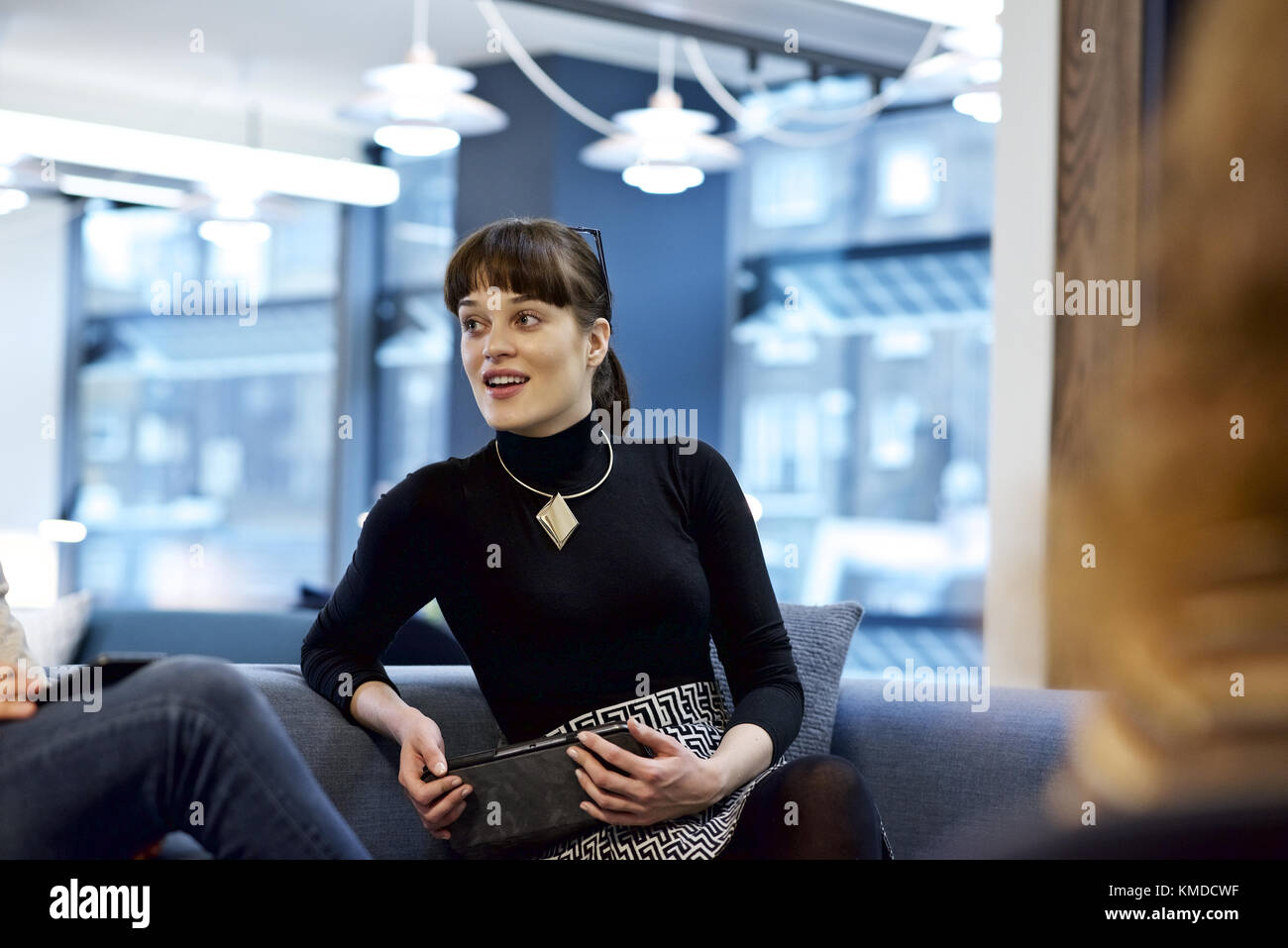 Kaukasische Geschäftsfrau mit einem mobilen Gerät und im Gespräch mit Kollegen vor der Kamera, in einem modernen Büro Stockfoto
