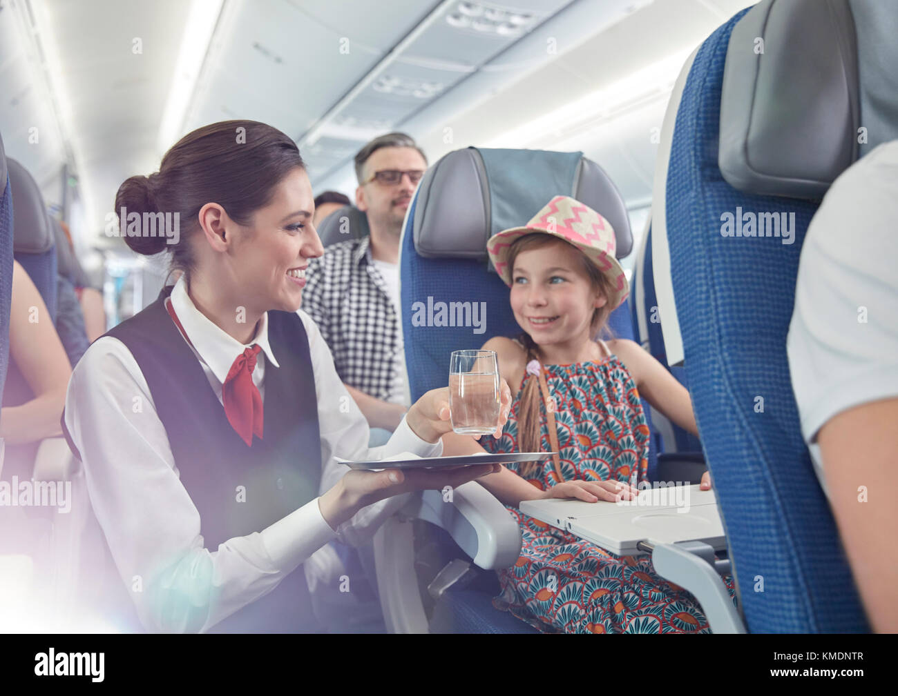 Weibliche Flugbegleiterin, die Mädchen im Flugzeug Wasser serviert Stockfoto