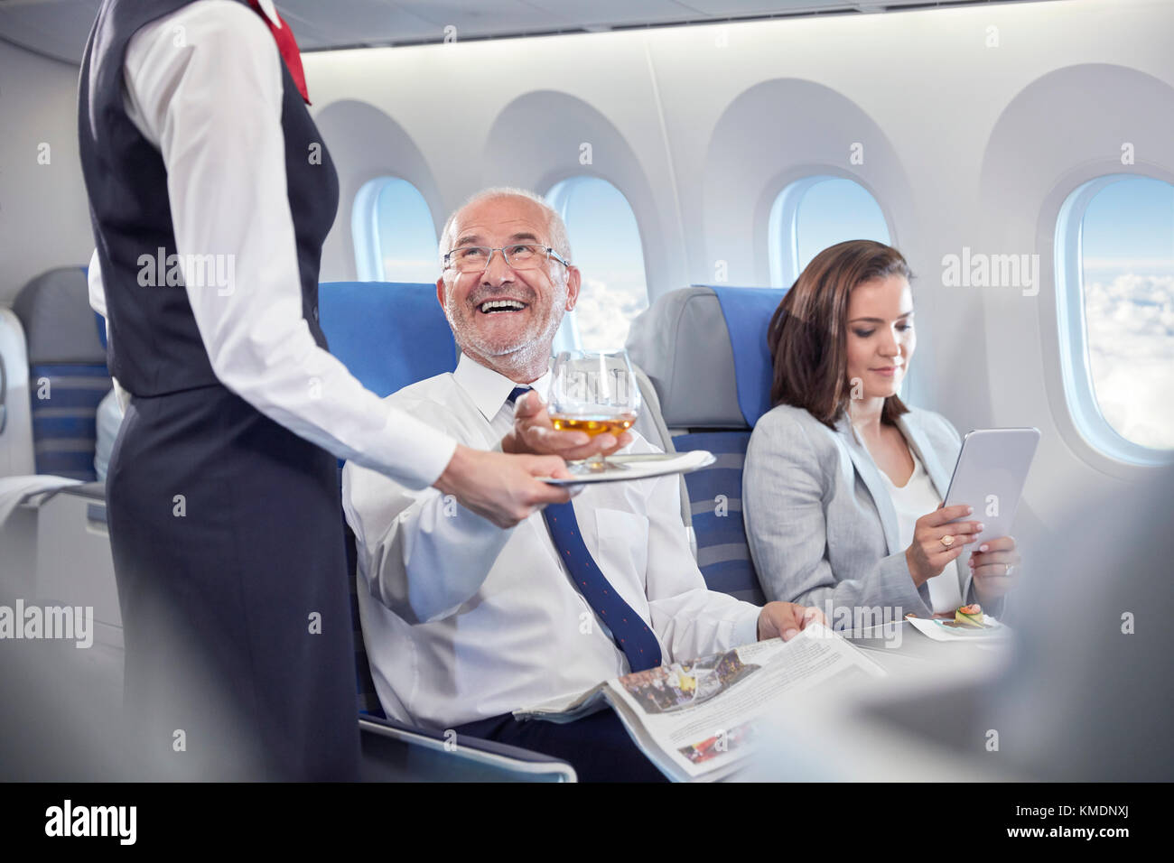Der Flugbegleiter serviert dem lächelnden Geschäftsmann, der zuerst auf der Fahrt ist, Whiskey Klasse im Flugzeug Stockfoto