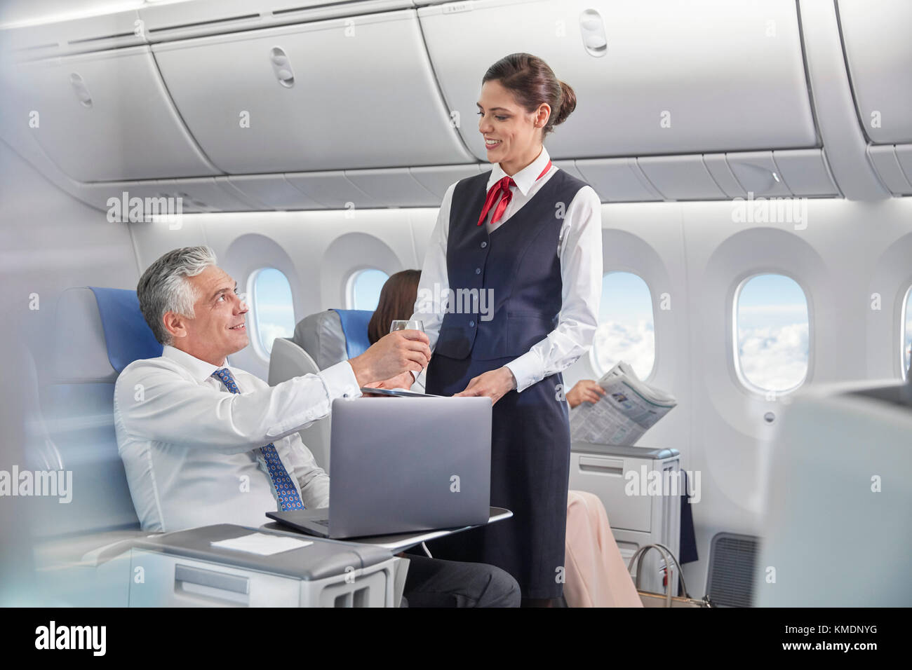 Ein Flugbegleiter serviert dem Geschäftsmann, der am Laptop arbeitet, Getränke Flugzeug Stockfoto