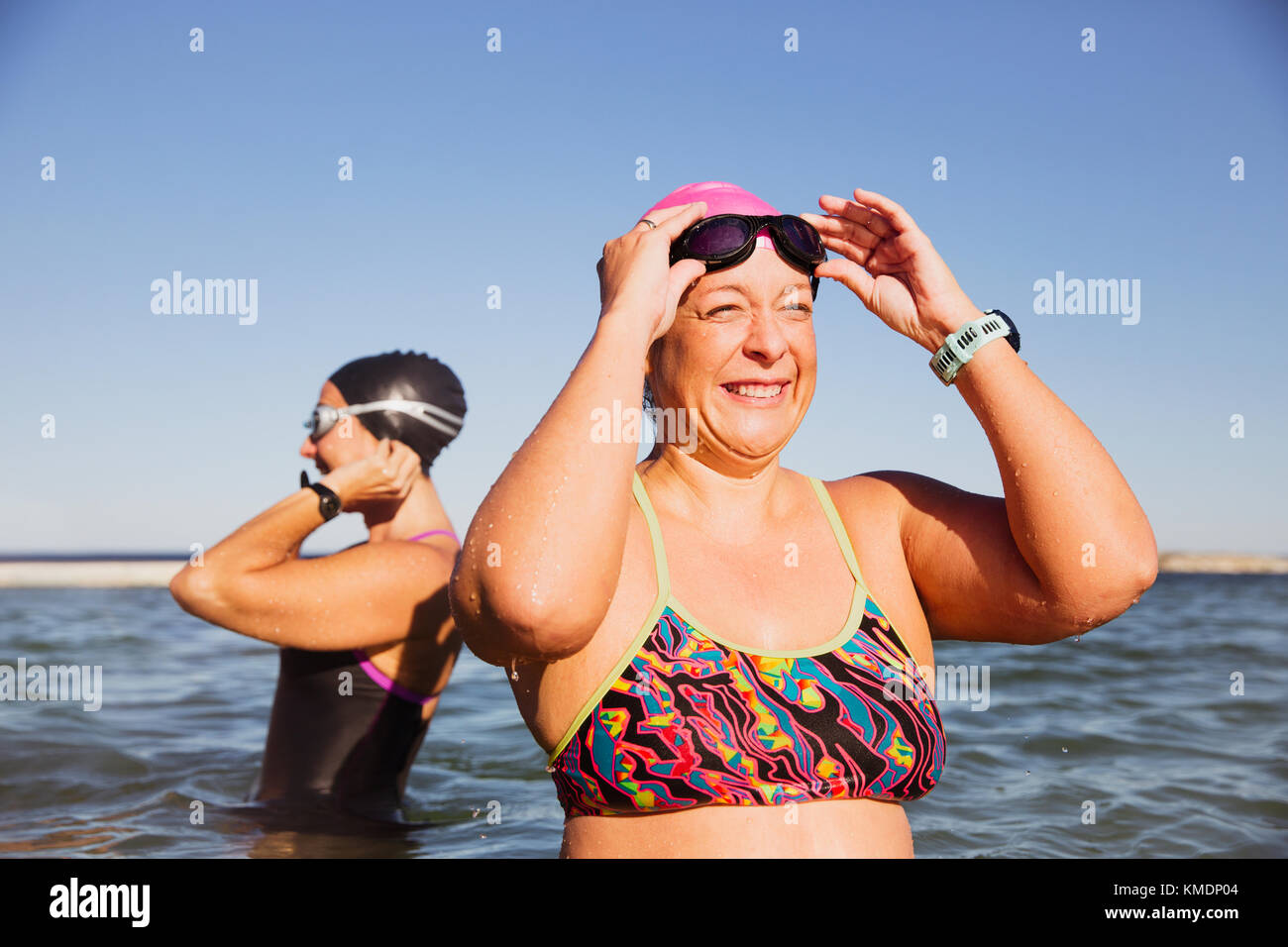 Lächelnde, glückliche Schwimmerin im offenen Wasser, die die Schwimmbrille im sonnigen Meer justiert Stockfoto