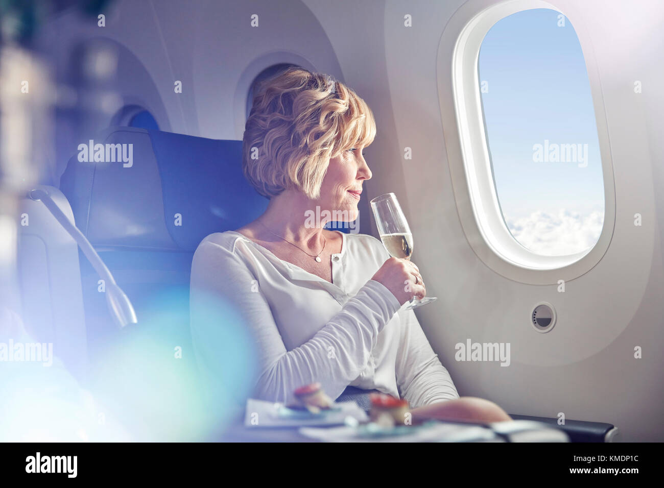 Reife Frau trinkt Champagner, Fenster in der ersten Klasse auf Flugmodus Stockfoto