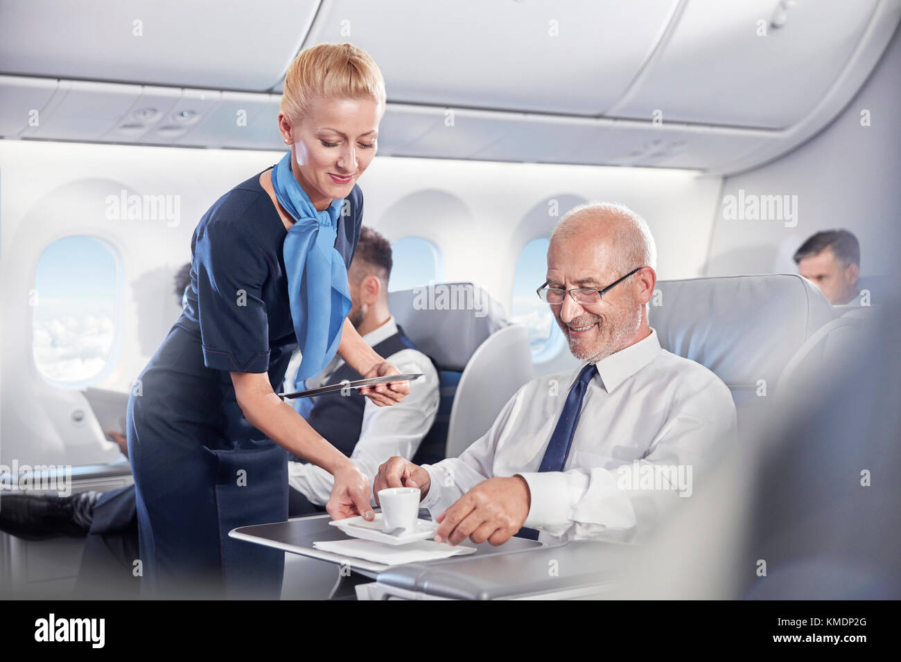 Flight Attendant serving Espresso, Geschäftsmann, der in der ersten Klasse auf Flugmodus Stockfoto