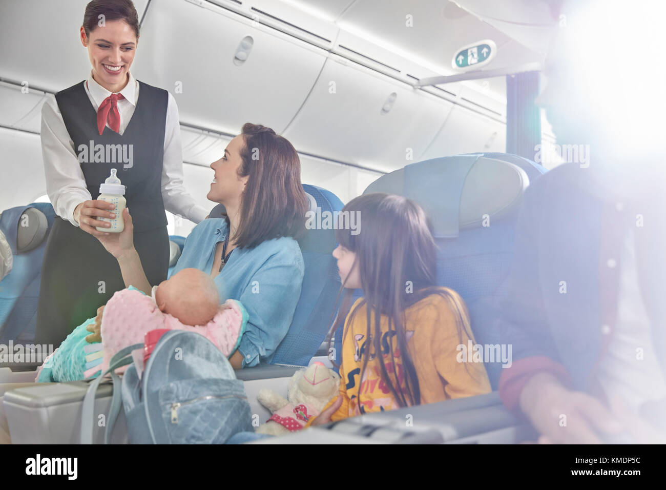 Lächelnder Flugbegleiter bringt Babyflasche zur Mutter mit Baby Im Flugzeug Stockfoto