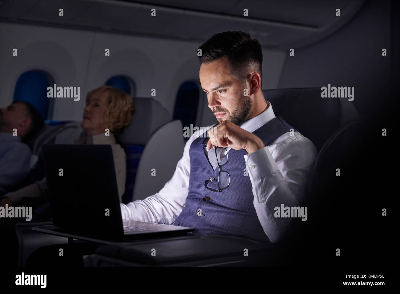 Seriöser Geschäftsmann, der am Laptop im Nachtflugzeug arbeitet Stockfoto