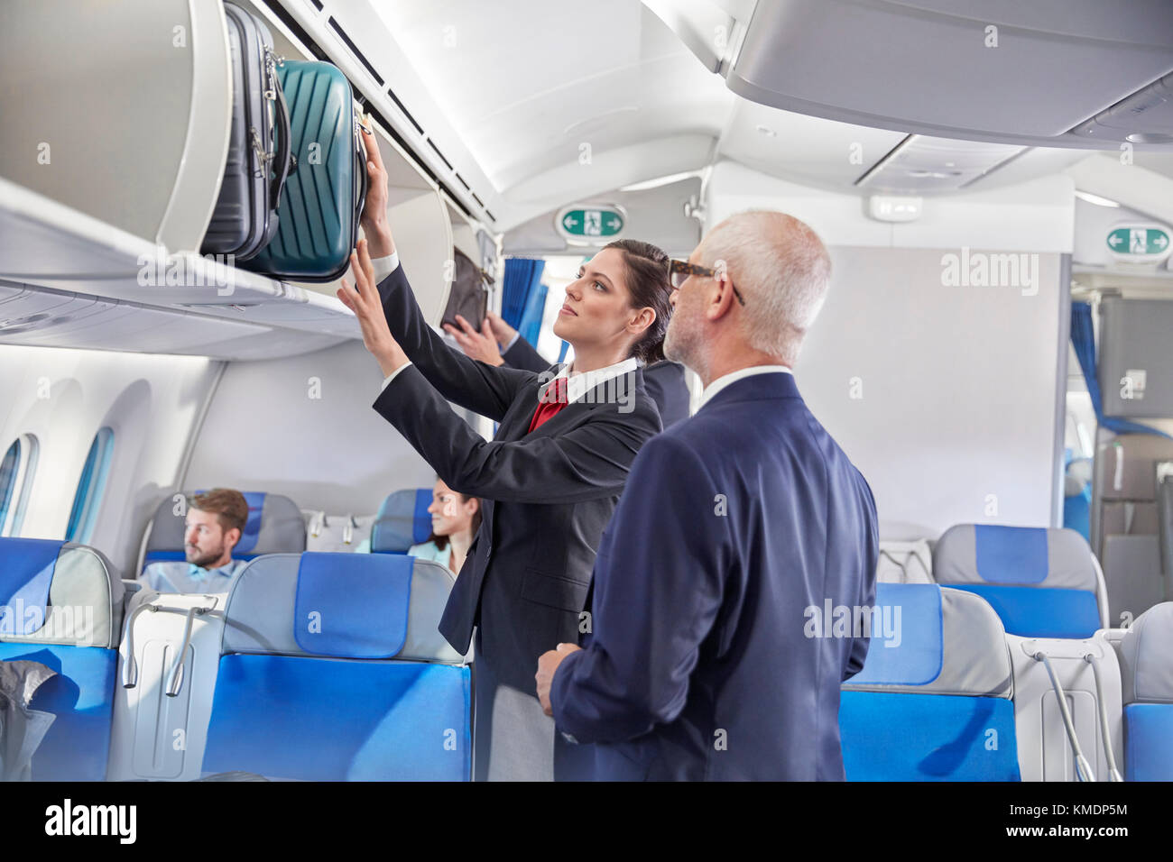 Der Flugbegleiter hilft dem Geschäftsmann, das Gepäck in den Gepäckraum zu legen Flugzeug Stockfoto