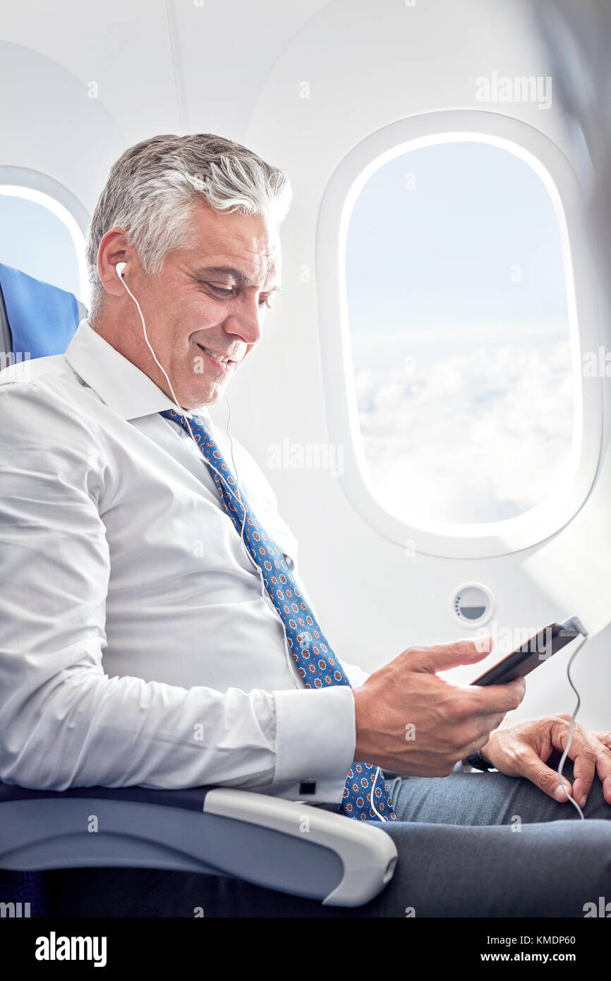 Geschäftsmann hört Musik mit Kopfhörern und MP3-Player an Flugzeug Stockfoto