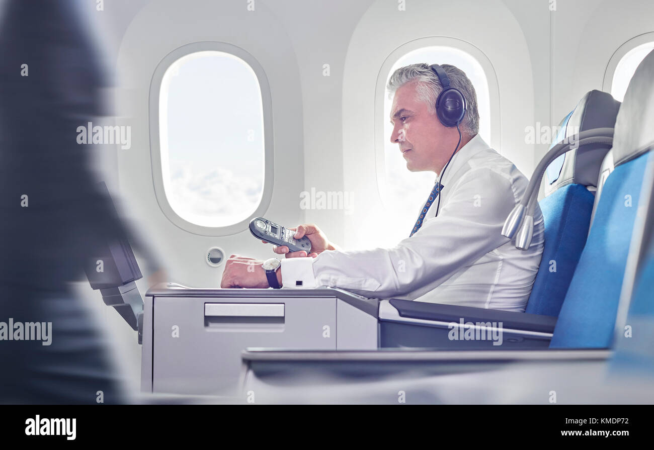 Geschäftsmann mit Kopfhörern und Fernbedienung, der Filme im Flugzeug ansieht Stockfoto
