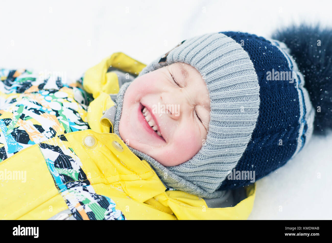 Kleiner Junge im Schnee spielen, Porträt, das Liegen auf dem Rücken und lacht Stockfoto