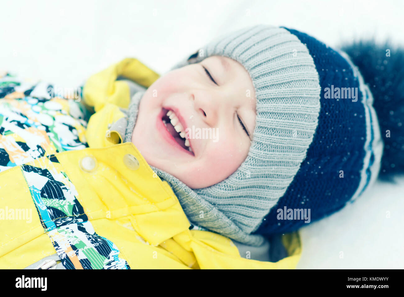 Kleiner Junge im Schnee spielen, Porträt, das Liegen auf dem Rücken und lacht Stockfoto