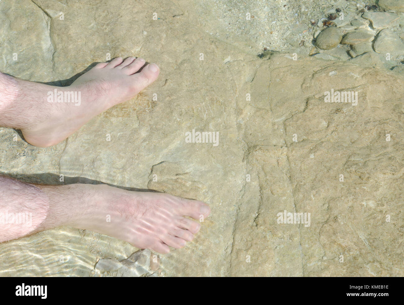 Zwei männliche Füße paddeln im sonnenverwöhnten Wasser des Gardasees bei Sirmione Stockfoto