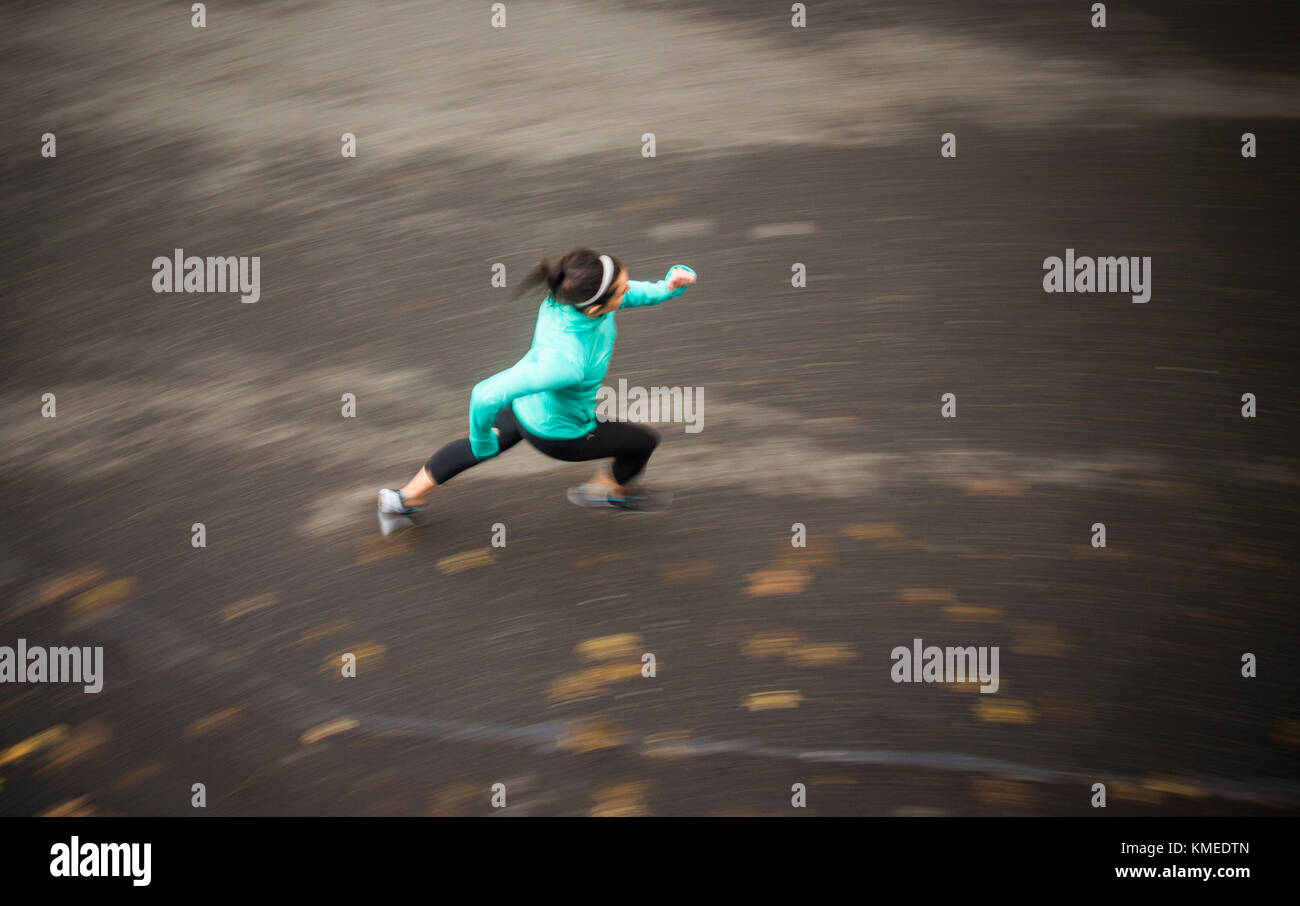 Ein verschwommenes Bild einer jungen Frau, die auf einer von oben aufgenommenen Straße läuft. Stockfoto