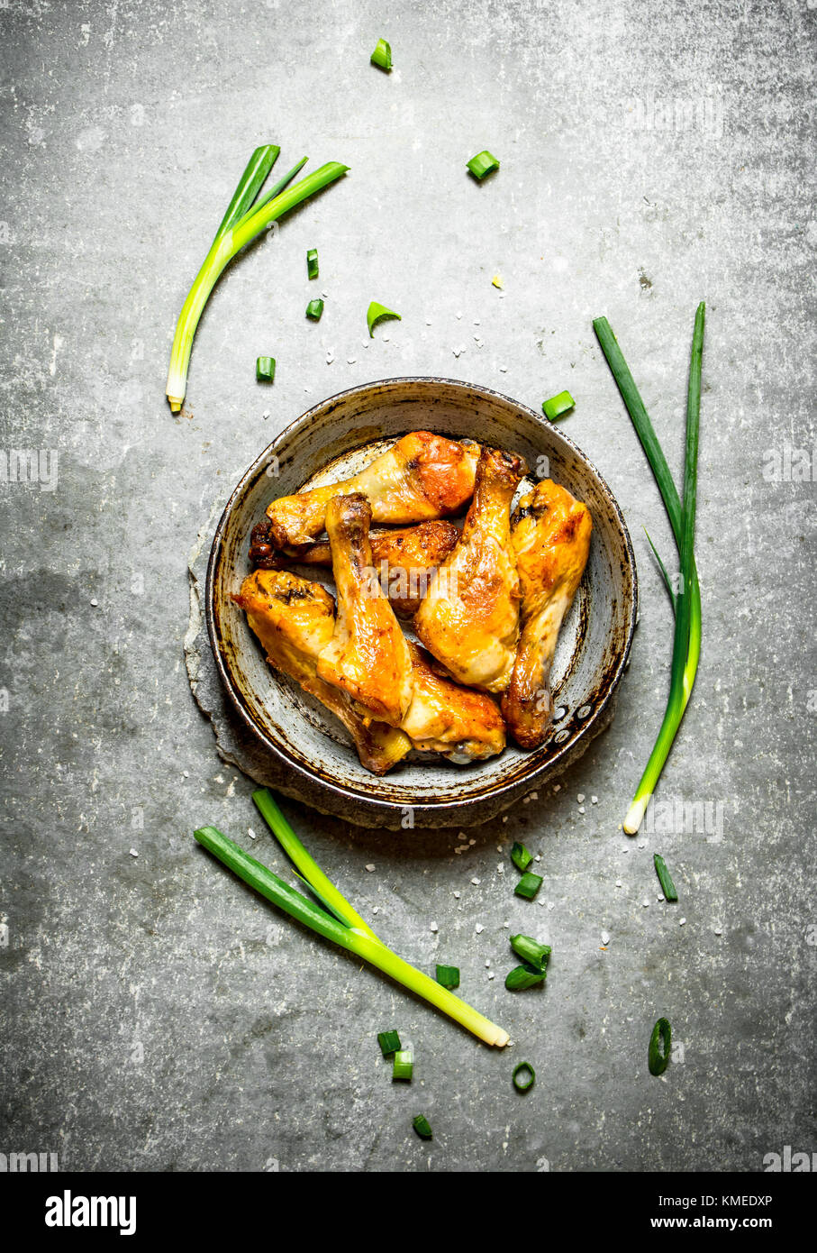 Hähnchenschenkel mit grünen Zwiebeln. Auf einem Stein. Stockfoto