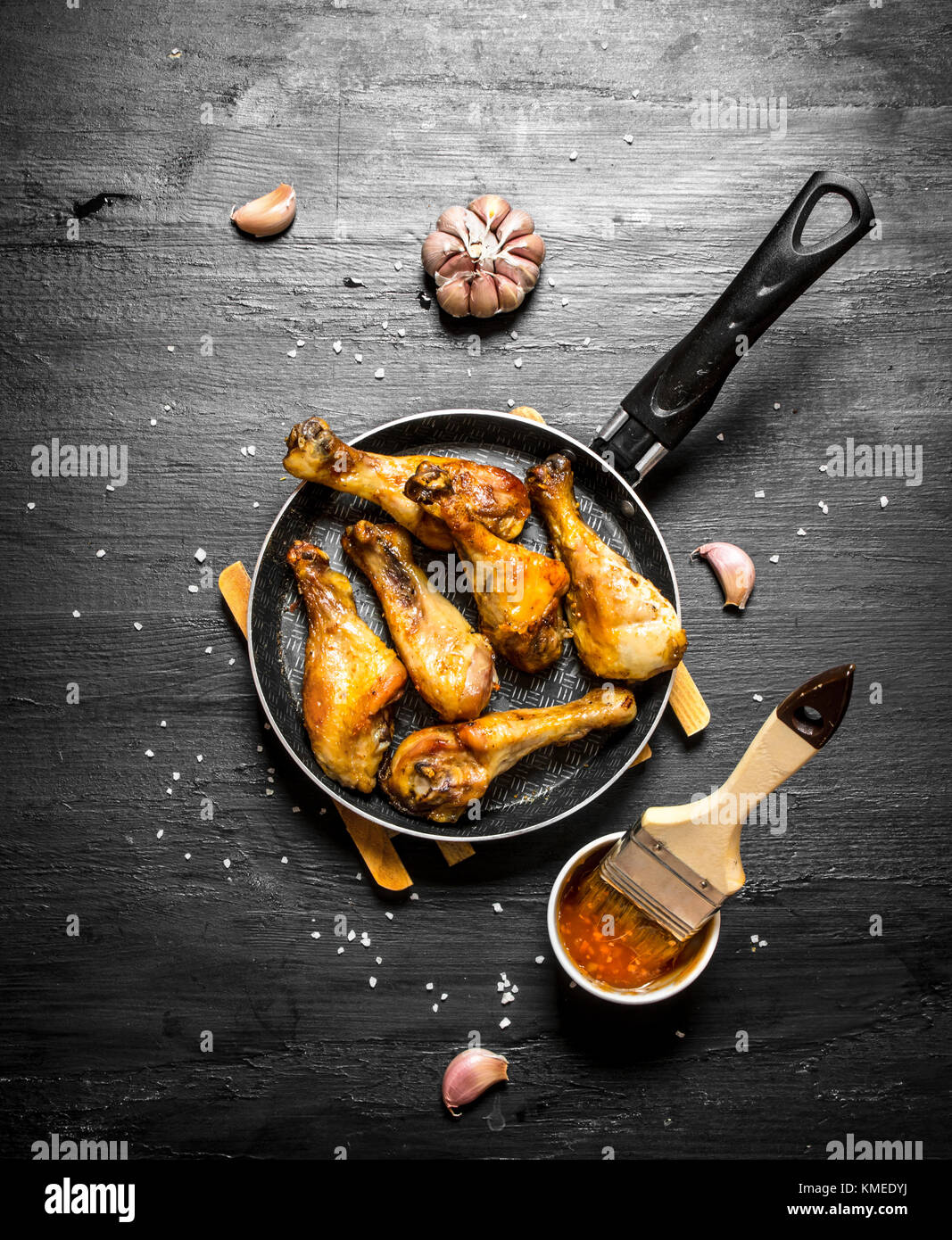 Gebratene Hähnchenkeulen mit Knoblauch und Soße. auf einem schwarzen Holz- Hintergrund. Stockfoto