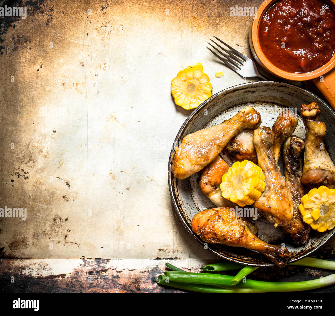 Hähnchenschenkel mit Mais und Tomatensauce. Auf einem alten rustikalen Hintergrund. Stockfoto