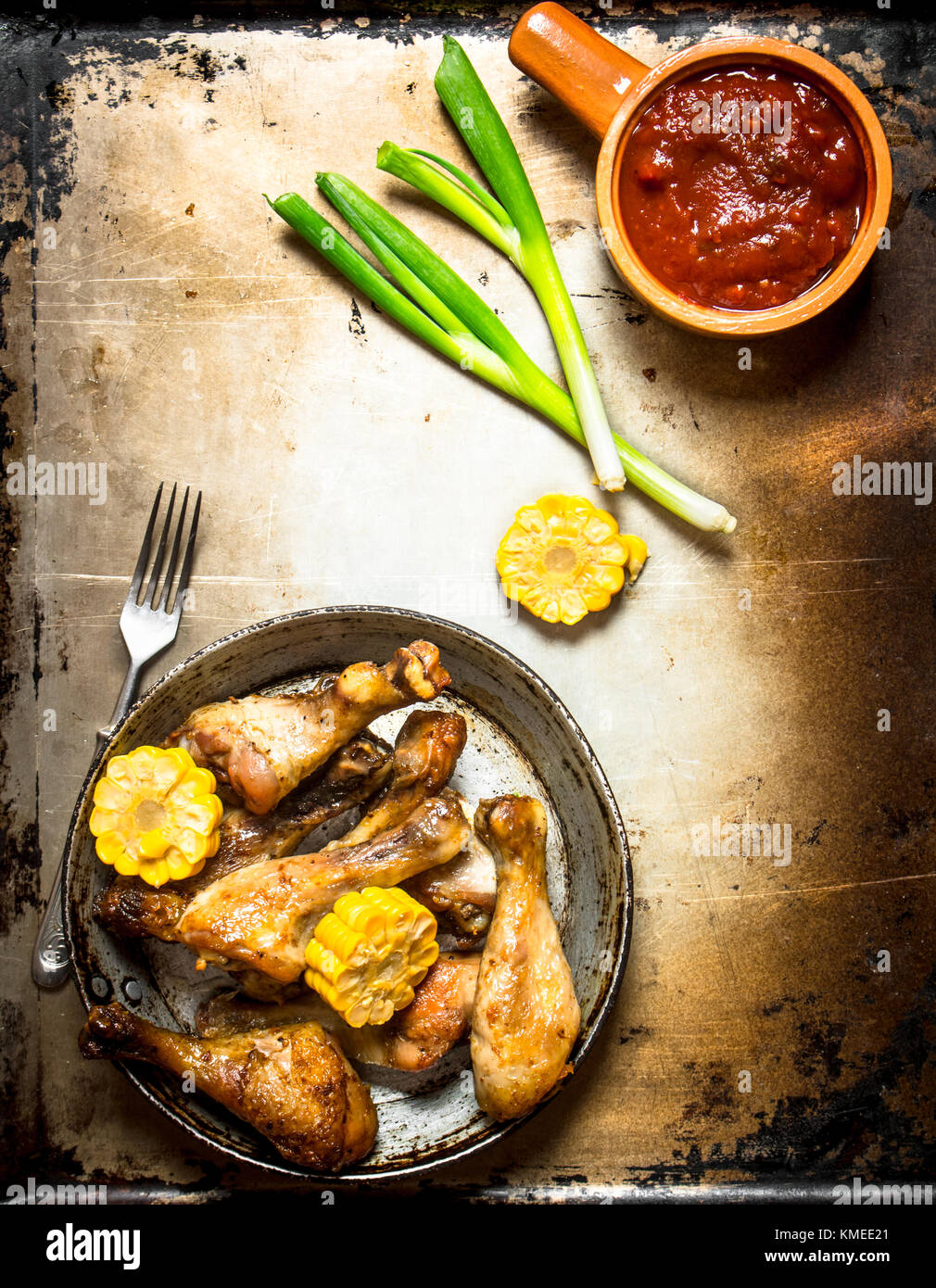 Hähnchenschenkel mit Mais und Tomatensauce. Auf einem alten rustikalen Hintergrund. Stockfoto