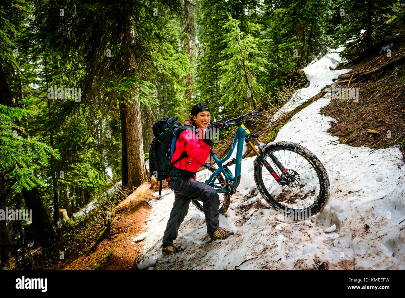 Weibliche Mountainbiker im Wald schiebt Bike wenn Schnee auf dem Eis Trail Seen, USA Stockfoto