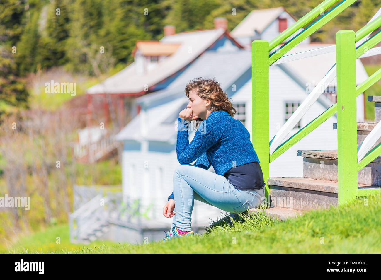 Junge Frau auf der Veranda der bunt bemalten Haus in idyllischer Landschaft Sommer Landschaft in Skandinavien und Kanada sitzen mit der Hand auf das Gesicht denken Stockfoto