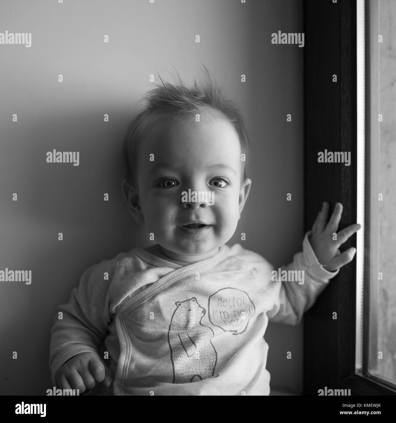 Porträt eines kleinen Jungen, der im Fenster sitzt und lächelt. Emotionen Konzept. Stockfoto