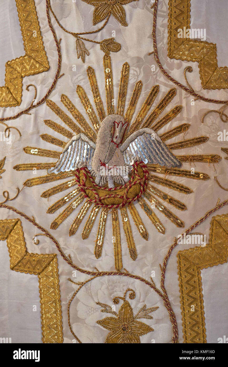 Ein dekoratives römisch-goldenes, römisch-katholisches Seidengewand, in dem die christliche Symbolmutter Pelican ihre drei jungen Küken füttert. Stockfoto