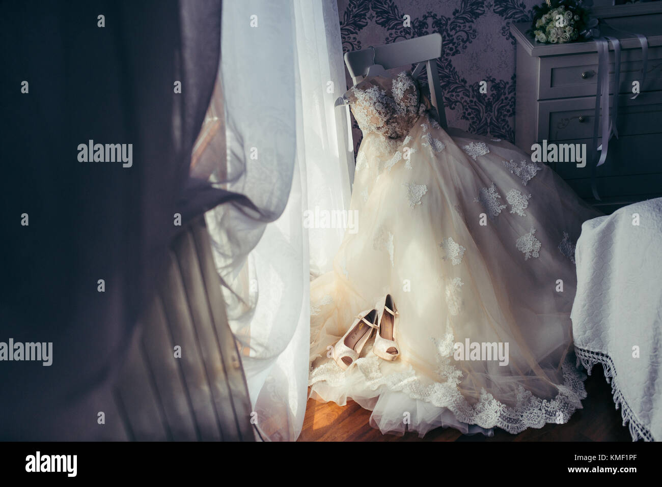 Die schönen langen Hochzeit Kleid mit Blumen hängen auf den weißen Stuhl in der eleganten Zimmer. Die beige High Heels auf dem Kleid platziert sind. horizontale Ansicht. Stockfoto