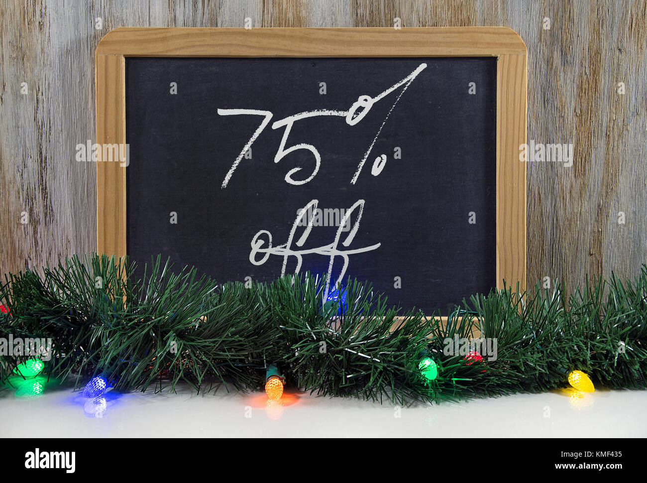 Weihnachten Verkauf Zeichen 75 Prozent Rabatt auf Schwarze Schiefertafel mit Holiday Lights und girlande auf glänzenden weißen Oberfläche Stockfoto