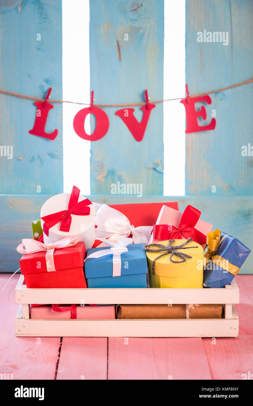Bündel von bunten präsentiert in einem weißen Holzkiste auf einem rosa Tabelle, mit dem Wort Liebe zu einer Zeichenfolge an einer blauen Holzzaun gebunden, im Hintergrund. Stockfoto