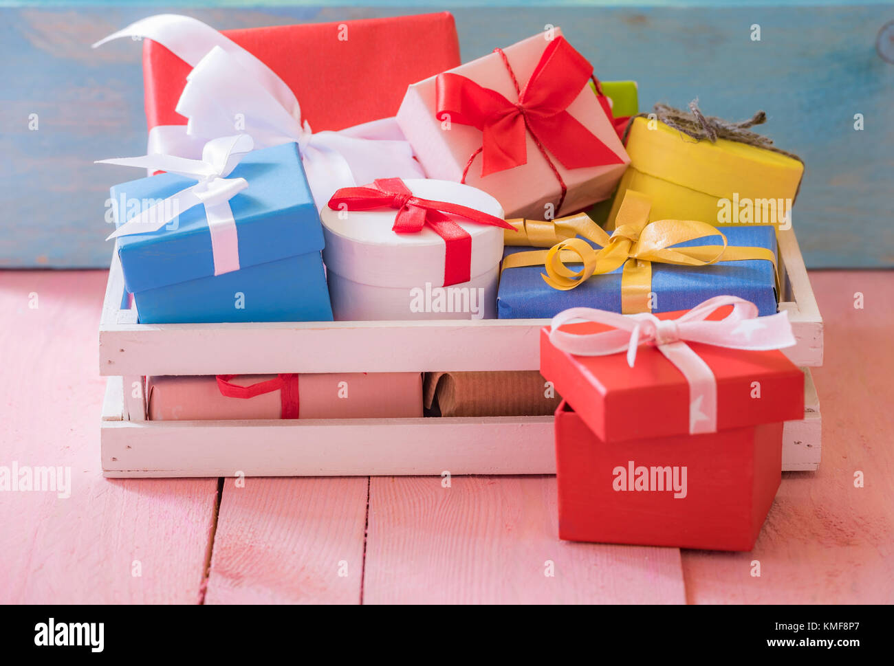 Gifting Thema Bild mit einem Haufen bunt eingepackten Geschenke, in einem weißen Holz- Krater, auf einer rosa Tabelle und ein blaues Holz- Hintergrund. Stockfoto