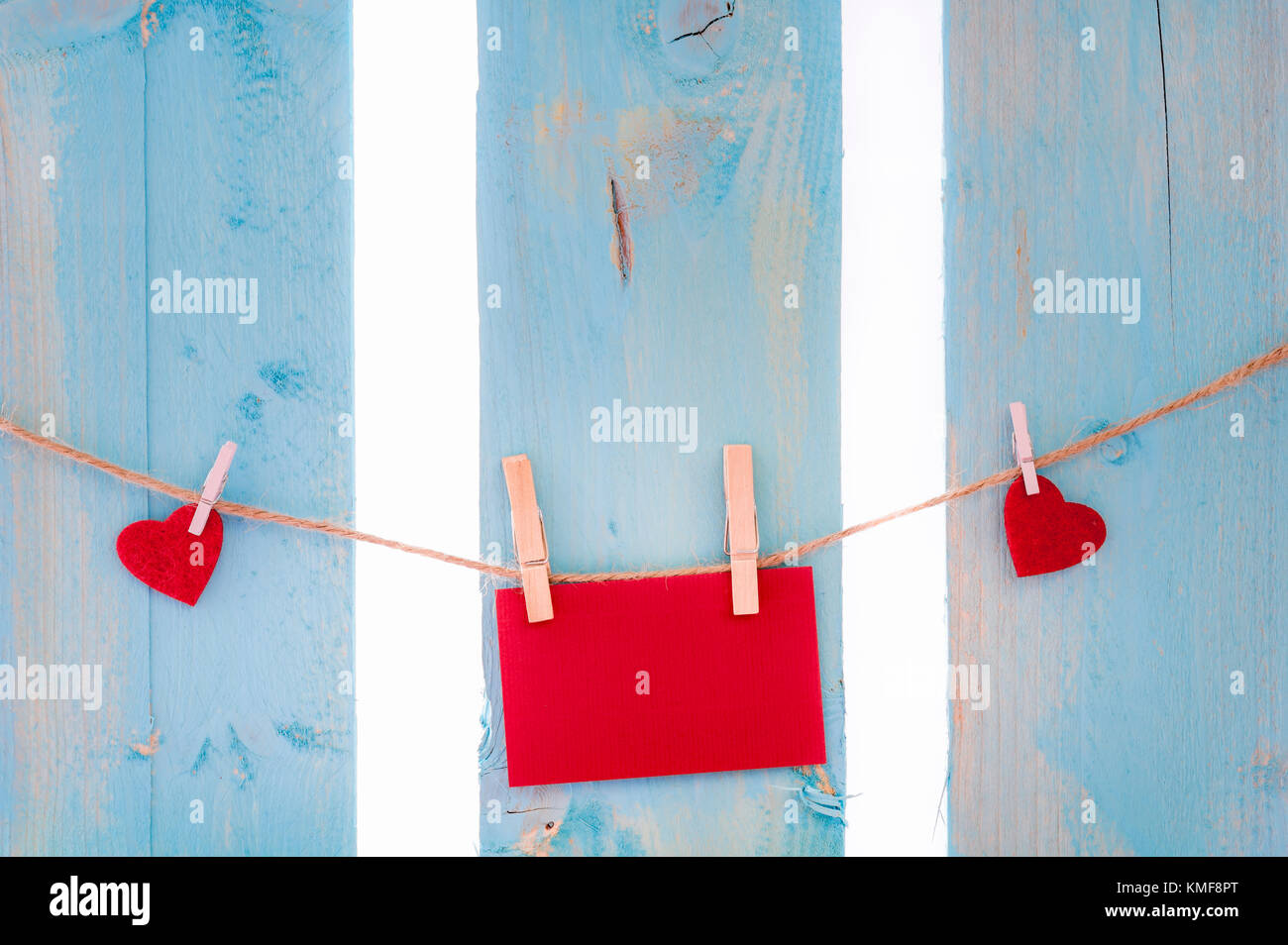 Leeres rotes Nachricht Karte mit roten Herzen, zu einem Leinen string mit Holz- Clips gebunden umgeben, auf einem blauen Zaun. Stockfoto