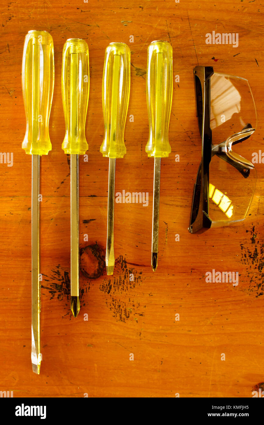 Blick von oben auf ein gelbes Schraubendreher Satz und Schutzbrille auf einem Holz Tisch Stockfoto